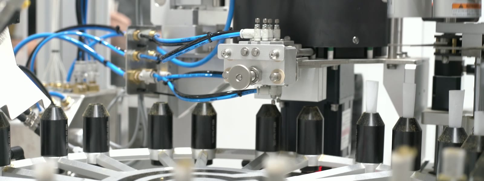 An AuraX rotary carousel indexing a full row of cones packed with ground flower past the filling manifold while white tips are seated into them.